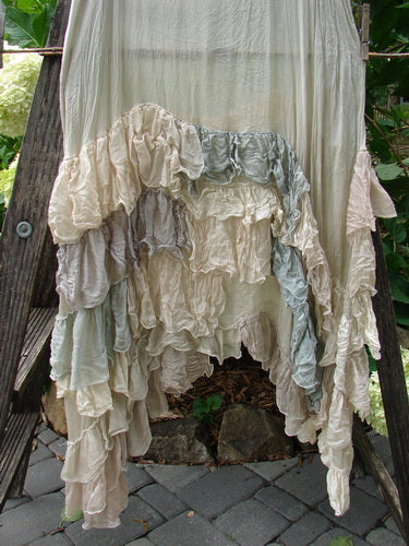 Magnolia Pearl Linen Voile Ruffle Pinafore displayed draped on a wooden ladder, highlighting its intricate ruffled design.