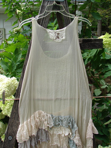 Magnolia Pearl Linen Voile Ruffle Pinafore Gray Silver Pastels OSFA dress hanging on a clothesline, showcasing its delicate ruffled fabric and elegant design.