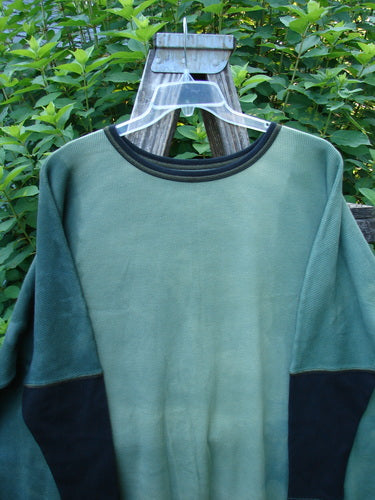 Barclay Thermal Contrast Revival Top Unpainted Mottled Field Moss OSFA displayed on a wooden fence, highlighting its ribbed sleeves, rounded neckline, and A-line shape, embodying Bluefishfinder.com's vintage, creative aesthetic.