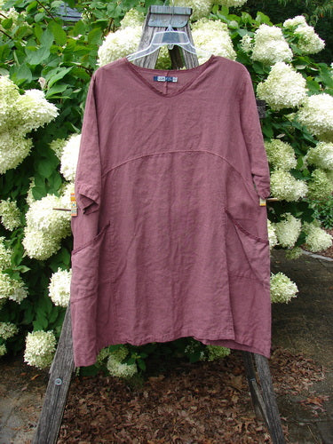 Barclay Summercloth Ditsy Trim Urchin Dress in unpainted loam, large size 0, shown as a loose mauve-brown dress with a rounded neckline, short sleeves, and a softly curved seam across the chest. The lightweight cloth hangs from a clear hanger against pale hydrangea blooms and weathered wood.