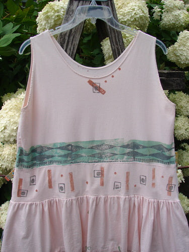 1990 The Tier Dress Polka Diamond Pink Peach OSFA in pale pink-peach, a sleeveless tiered dress with a scoop neckline and gathered waist. The soft, lightweight fabric is patterned with small diamond and dot motifs, plus a teal geometric band across the middle.