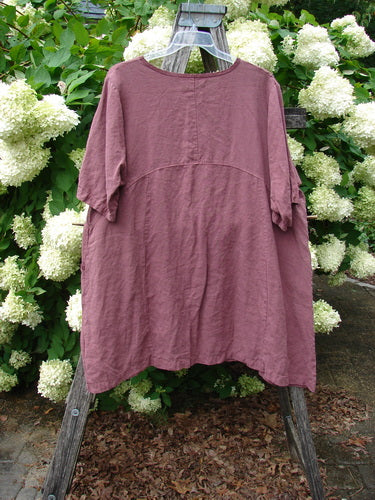 Barclay Summercloth Ditsy Trim Urchin Dress in unpainted loam, large size 0, hangs from a weathered wooden stand. The loose, short-sleeve dress has a softly curved seam, a relaxed drape, and a matte, textured finish, set against dense white hydrangeas and green foliage.