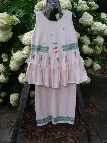 1990 The Tier Dress Polka Diamond Pink Peach OSFA in pale pink-peach, a sleeveless tiered dress with a scoop neck, scattered tiny diamond and polka motifs, teal horizontal bands, and a ruffled lower tier. The lightweight fabric hangs from a wooden ladder outdoors, framed by dense white hydrangeas and dark greenery.