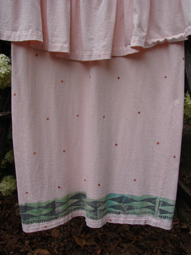 1990 The Tier Dress Polka Diamond Pink Peach OSFA in soft pink-peach fabric, with a tiered hem and scattered tiny polka-diamond dots. A green geometric border trims the lower edge, while the dress hangs straight in a close crop with muted, natural light.