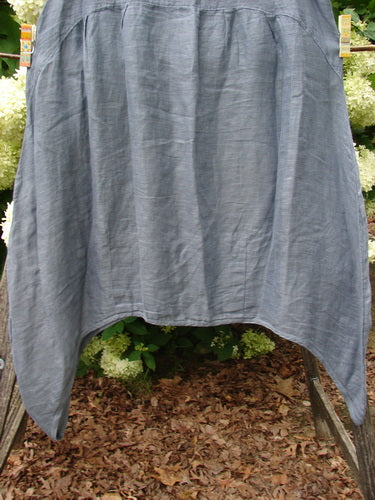 Barclay Linen Tuesday's Dress Guinea Feather Grey Storm, size 0, in a feather gray linen with a softly wrinkled texture and loose, draped silhouette. The garment hangs outdoors between supports, with a wide curved hem and airy, translucent folds.