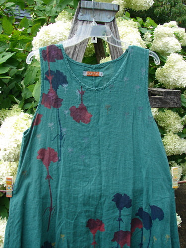 Barclay Linen Round Bottom Pinafore in Cloud Burst Jade, size 0, with a sleeveless A-line shape and round neckline in textured jade linen. Dark red and navy floral motifs trail across the front, hanging from a clear hanger amid white hydrangeas.