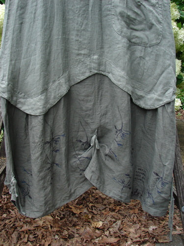 Barclay Linen Explorer Jumper in buttercup green, River size 0, with layered linen panels, a rounded hem, and a gathered center tie over a darker printed underlayer. The loose drape and soft matte texture fill the frame in muted green-gray tones.