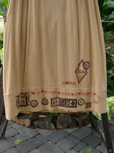 1998 Scrabble Skirt Games Bamboo Size 2: Close-up of a tan, mid-weight organic cotton skirt with horizontal panels, flat folded waistline, and classical games theme paint. Features two upper finger pockets and a wide lower sweep.