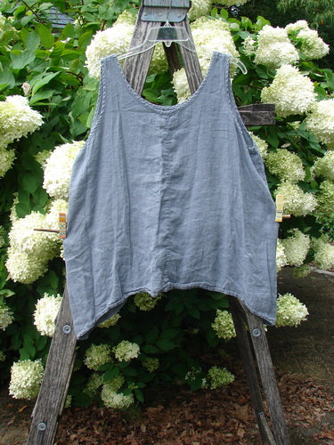 Barclay Linen Altoll Top Pansy Patch in blue dust, size 0, is a sleeveless linen top with a softly crinkled texture, wide scoop neckline, and relaxed A-line shape. It hangs on a weathered wooden ladder before dense white hydrangeas and deep green foliage.