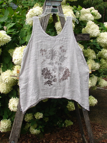 Barclay Linen Altoll Top Floral Victorian Floral Natural Size 0 in light natural linen, a sleeveless scoop-neck top with a soft drape and faded floral print. It hangs centered on a rustic wooden ladder amid white hydrangeas and green foliage.
