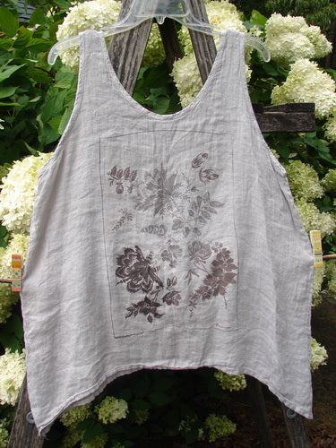 Barclay Linen Altoll Top Floral Victorian Floral Natural Size 0, a natural linen tank with a relaxed A-line shape, wide straps, and a deep scoop neckline. A muted Victorian floral print sits centered on the front, while the lightweight woven texture and soft drape are shown against leafy hydrangeas.