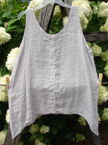 Barclay Linen Altoll Top Floral Victorian Floral Natural Size 0, a sleeveless natural linen top with a soft V neckline, wide straps, and an airy A-line drape. It hangs centered against dark wood and pale hydrangeas, its lightly wrinkled texture and muted gray-beige tone clearly visible.