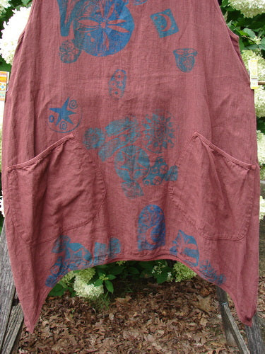 Barclay Summercloth Round Pocket Pinafore Star Flower Rusty Bucket Size 0 in faded rust, a soft, crinkled sleeveless pinafore with rounded patch pockets and blue star-and-flower prints. It hangs loosely outdoors, revealing a relaxed A-line shape and worn texture.