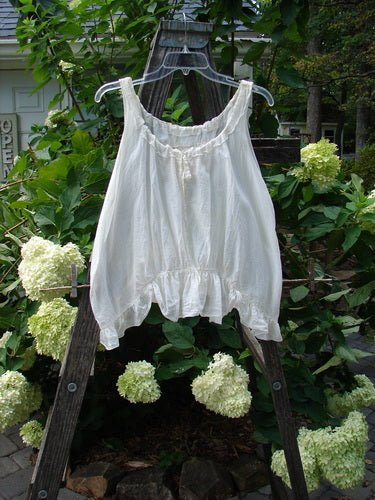 Magnolia Pearl Silken Cotton Voile Ribbon Neck Top White OSFA displayed on a hanger, showcasing its delicate ribbon neckline, tiny pearl buttons, and flutter hemline.