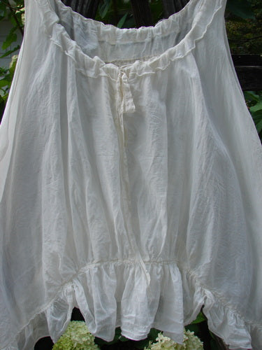 Magnolia Pearl Silken Cotton Voile Ribbon Neck Top White OSFA on a clothes rack, featuring a flutter hemline, adjustable neckline with silk ribbon, and tiny pearl buttons.