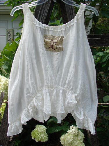 Magnolia Pearl Silken Cotton Voile Ribbon Neck Top White OSFA, hanging on a rope, showcasing its adjustable neckline with silk ribbon, tiny pearl buttons, flutter hemline, and signature Magnolia Pearl love patch.