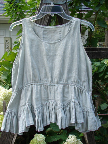 Magnolia Pearl Linen Roman Ruffle Top Light Sage OSFA displayed on a hanger, showcasing a rounded neckline, scalloped hemline, and double scooped waist seams, reflecting vintage-inspired design from Bluefishfinder.com.