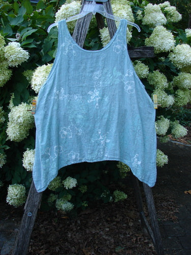 Barclay Linen Altoll Top Falling Floral Sage, Size 2, is a loose, sleeveless sage top with a soft linen texture and subtle falling floral pattern. It hangs from a wooden ladder against white hydrangeas, its airy drape and curved hem clearly visible.