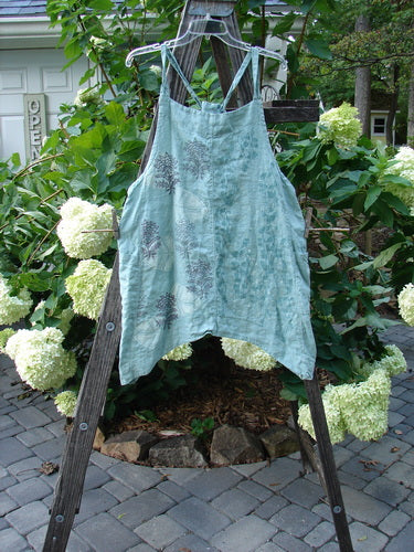 Barclay Linen Side Pocket Apron Jumper with Fan Floral design in Dusty Sage, displayed draped over a wooden ladder, highlighting its sectional panels and wrap side drop pockets.