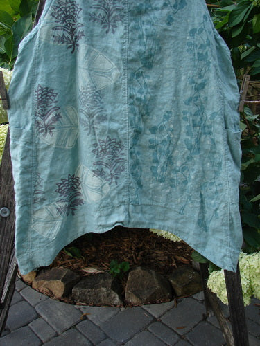 Barclay Linen Side Pocket Apron Jumper in Dusty Sage with fan floral pattern, displayed on a clothes rack, showcasing its sectional panels, side pockets, and adjustable shoulder straps.