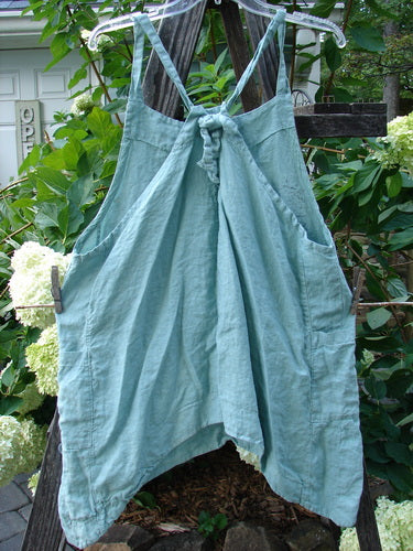 Barclay Linen Side Pocket Apron Jumper in Dusty Sage, featuring a fan floral pattern, hung on a clothesline outdoors with visible adjustable shoulder straps and sectional panels.