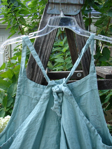 Barclay Linen Side Pocket Apron Jumper Fan Floral Dusty Sage Size 0 displayed on an outdoor swing, showcasing sectional panels, wrap side drop pockets, and adjustable shoulder straps.