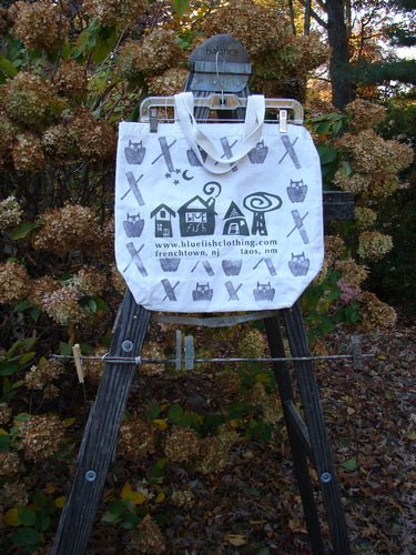 A white tote bag with black and white designs featuring the Blue Fish Barclay Shops owls and village logo. Made from lightweight cotton canvas with a shorter shoulder strap, generous top opening, and deeper rounded bottom. Perfect size for everyday use.