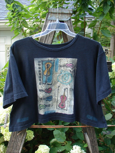 1991 Crop T Top Music Days Black OSFA displayed on a hanger, featuring a rolled neckline, cropped length, short sleeves, and vintage music-themed print, highlighting Blue Fish's unique, collectible style.