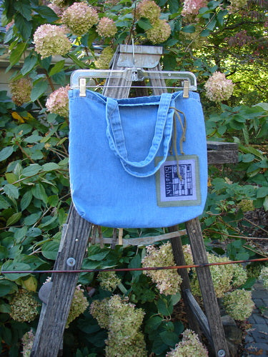 2000 PMU Cotton Tote Bag Summer Floral Pocket Washed Denim One Size displayed on a wooden ladder, showcasing tote length shoulder straps, colorful floral patches, and a center front pocket.