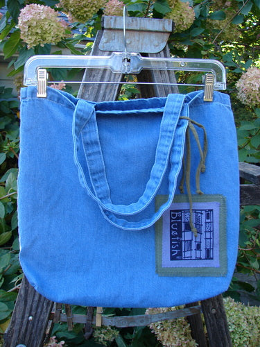 2000 PMU Cotton Tote Bag Summer Floral Pocket Washed Denim One Size displayed on a swinger, featuring tote-length shoulder straps, a gusset bottom, and colorful floral patches with a center front pocket.