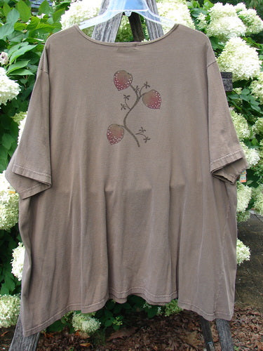 Barclay Short Sleeved Studio Tee Tree Offer Fauna Size 3 in muted taupe, a loose short-sleeved T-shirt with a soft, worn cotton look and a centered tree-and-berries graphic. It hangs from a white hanger outdoors against dense green foliage and white blossoms.