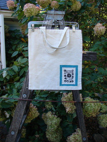 2000 PMU Patched Cotton Canvas Pocket Tote Promo Natural One Size displayed on a wooden stand, showcasing its organic cotton canvas with fringe and colorful accents, emphasizing sustainable upcycling by Bluefishfinder.com.