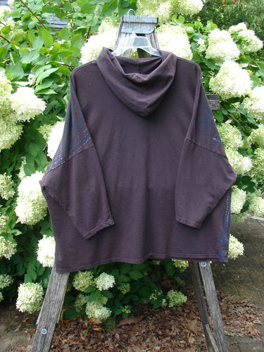 Barclay Cotton Lycra Dolman Roo Pocket Hoodie in Pansy Rose Deep Bark, OSFA, shown in a deep bark hue with a relaxed dolman shape, hood, and roomy front pocket. The soft cotton-lycra fabric drapes loosely on a hanger against dense white hydrangeas and green foliage.
