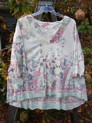 Magnolia Pearl European Cotton Breeze Blouse Spring Florals OSFA, featuring a soft floral print and feathery raw edges, displayed on a hanger showcasing its rounded A-line shape and varying hemline.