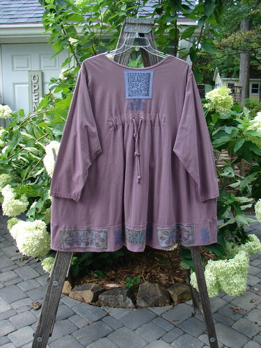 1993 Modernismo Cardigan in Plum Wine Size 2 displayed on a rack, featuring nature-themed paint, old-timey buttons, front kangaroo pockets, drawcord back, oversized signature patch, and thicker banded hemline.