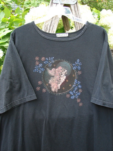 Barclay Short Sleeved Studio Tee Magic Moon Cloud in black, size 3, is a dark short-sleeved T-shirt with a round neckline and a central moon-and-cloud graphic in pink, blue, and brown. The cotton fabric hangs softly against a hanger, with leafy greenery behind it.