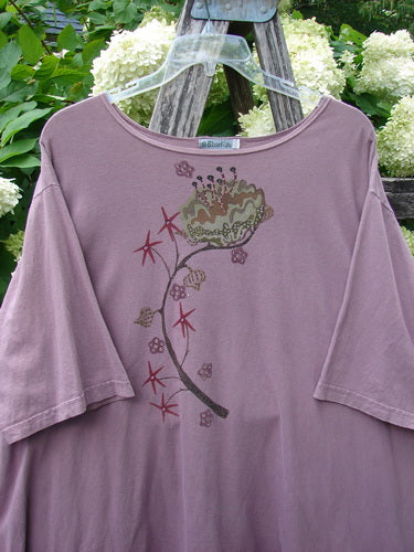 Barclay Short Sleeved Studio Tee Tree Star Laurel Size 3 in muted mauve, a loose short-sleeve T-shirt with a soft matte knit and wide neckline. A curved tree-and-star floral graphic trails down the front, hanging on a clear hanger against leafy greenery.