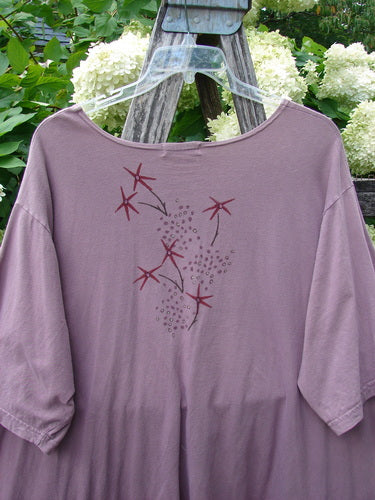 Barclay Short Sleeved Studio Tee Tree Star Laurel Size 3 in muted lavender, a loose short-sleeve tee with a wide neckline and soft drape. The front shows a delicate tree-star laurel graphic in burgundy and gray, hanging on a clear hanger against leafy greenery.