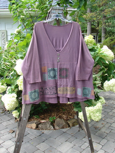 1993 Modernismo Pullover Cardigan Nature Plum Wine Altered Size 2 displayed on a hanger with visible kangaroo pockets, trio of decorative buttons, and oversized patch in an outdoor garden setting.