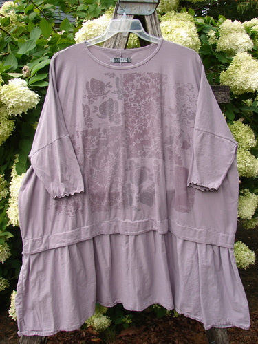 Barclay Batiste Banded Flounce Esperanza Tunic in Strawberry Garden Sea Fog OSFA, a loose lavender-gray top with a round neckline, wide banded sleeves, and a flounced hem. Soft crinkled fabric and faded floral print give it a layered, airy look.