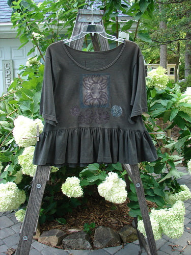 1992 Holiday Short Sleeved Peplum Top Black Sand Size 1 displayed on a wooden ladder, showcasing its ribbed neckline, drop shoulders, and peplum lower, crafted from mid-weight cotton jersey.