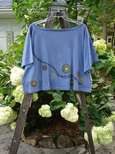 1993 Travel Top Pinwheel Periwinkle Size 2 on wooden ladder, showcasing a deeply scooped neckline, crop shape, chain and pinwheel paint, Blue Fish 93 patch, and ceramic glazed buttons.