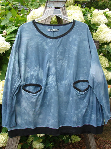 Barclay Cotton Lycra Open Rib Pocket Pullover in unpainted mottled blue shore, OSFA, with a loose drape, wide black ribbed neckline, and two oval front pockets trimmed in black. The cotton-lycra fabric has a soft, tie-dyed texture and hangs against a leafy outdoor backdrop.