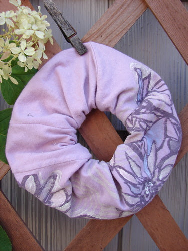 Barclay PMU Organic Cotton Hair Scrunchie Floral Lavender One Size, featuring ruffled fabric with a floral design, hangs on a wooden fence, showcasing its sustainable creation through Bluefishfinder.com's PatchMeUp Program.