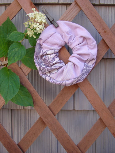 Barclay PMU Organic Cotton Hair Scrunchie Floral Lavender One Size, featuring ruffled fabric and floral design, displayed on a wooden lattice, highlighting its sustainable and vintage-inspired craftsmanship from Bluefishfinder.com.