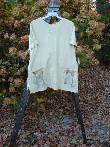 Barclay Short Sleeved Pocket Vent Tunic Top Celebrate Plantain Size 0: A white shirt on a clothes rack with short sleeves, tall side vents, and two drop exterior pockets.