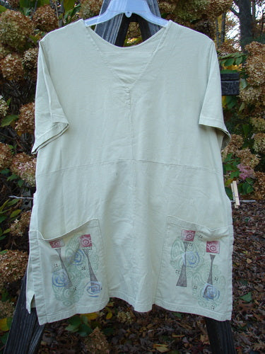 A white short-sleeved tunic with a unique triangular neckline insert, tall side vents, and two drop exterior pockets. Made from organic cotton, this Barclay Short Sleeved Pocket Vent Tunic in Plantain is from a Summer Collection.
