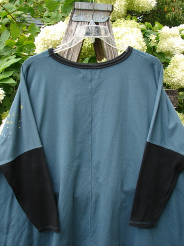 Barclay Cotton Lycra Rib Sleeved Treesoul Pullover in Orchid Forest, OSFA, shown on a clear hanger outdoors. The blue-green pullover has a ribbed black crew neckline and long black sleeves, with a soft cotton-lycra drape and a few small yellow marks near the left shoulder.