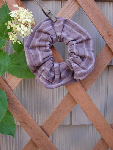 1999 PMU Organic Cotton Hair Scrunchie Unpainted Grey Plum Stripe One Size displayed on a wooden lattice, showcasing its soft ruffled fabric and sustainable design from Bluefishfinder.com’s vintage-inspired collection.