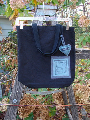 1994 PMU Patched Tote Bag Wood Path Black One Size displayed on a wooden ladder, featuring long shoulder straps and a colorful heart patch, embodying sustainable vintage design.